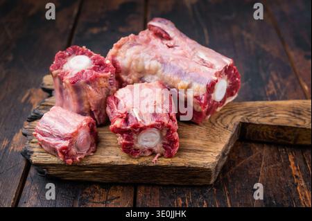 Lamb oxtail sections ready for cooking with herbs on wooden cutting board, overhead composition on dark wood surface. Stock Photo