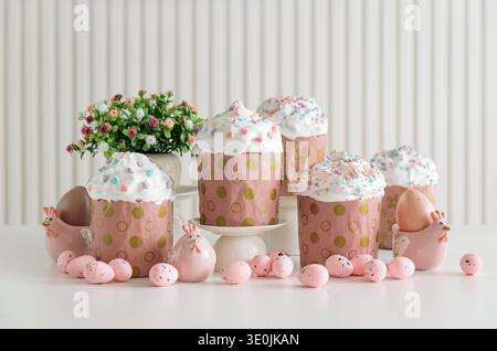 Festive Easter cakes with white frosting and colorful sprinkles in pink wrappers with gold polka dots, surrounded by colorful pastel eggs on white tab Stock Photo
