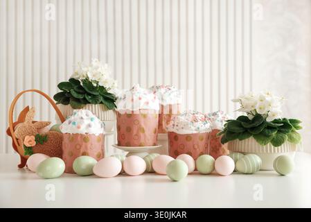 Festive Easter cakes with white frosting and colorful sprinkles in pink wrappers with gold polka dots, surrounded by colorful pastel eggs on white tab Stock Photo