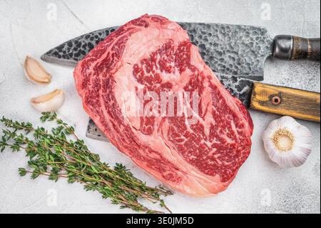 Premium raw ribeye beef steak with intense marbling and thick fat cap. Rustic butcher style on light stone background. Stock Photo