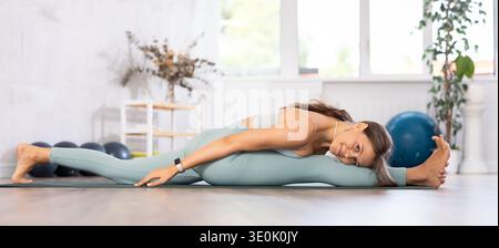 Young woman yoga trainer performing split pose pose on black rug Stock Photo