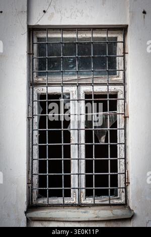 Broken window with iron bars in an abandoned or prison-like building Stock Photo