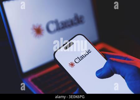 Izmir, Turkey - Mar 13 2026: Hand holding a modern smartphone with Claude AI app open on screen, modern laptop in background also showing Claude inter Stock Photo