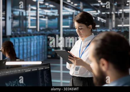Engineers using tablet in data center, managing server virtualization, running scripts. Woman in server farm using programming language on device to finetune network protocols Stock Photo