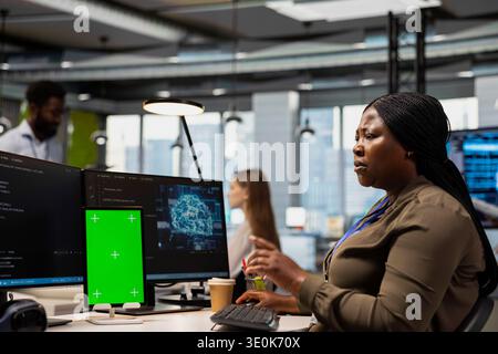 Admin in office uses green screen tablet, automating repetitive tasks with AI scripts. African american IT expert using artificial intelligence tech on mockup device to speed up feature implementation Stock Photo