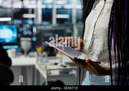 Close up of engineer in server room using tablet to review infrastructure diagnostics. IT professional in data center analyzing performance data using device to maintain system uptime Stock Photo