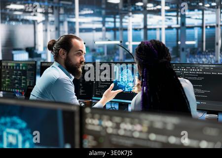 Data center coworkers doing brainstorming, working on databases supporting AI apps. Server room IT staff members cooperating, using artificial intelligence technology to do algorithms improvements Stock Photo