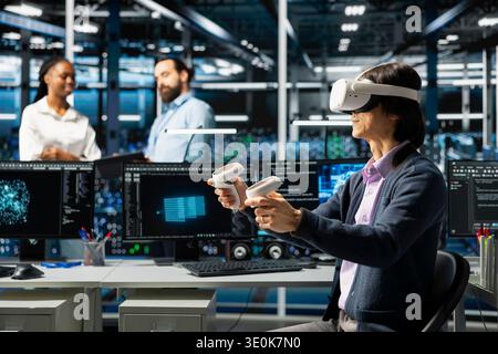 Data center programmer using VR headset, working on databases supporting AI apps. Server room worker using virtual reality an artificial intelligence to do algorithms improvements Stock Photo