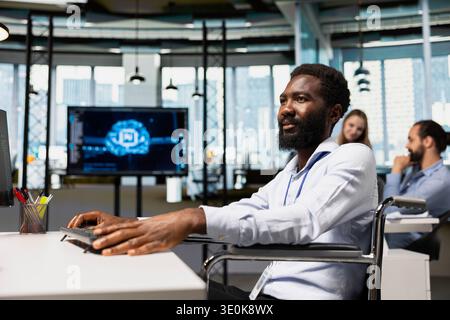 Engineer in wheelchair speeds up tasks by following AI language model suggestions in office. Worker with paraplegia in inclusive office relying on artificial intelligence LLM assistant to fix mistakes Stock Photo