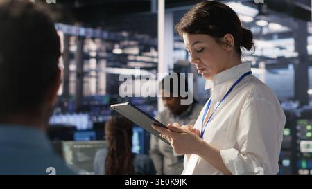 Data center team leader supervising system operations supporting neural networks and analytics workflows. Server hub manager monitoring engineering team managing AI training datasets, camera A Stock Photo