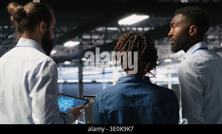 Data center manager talking with workers performing maintenance on supercomputers used for AI. Server hub team leader and staff members upgrading rigs used for deep learning training Stock Photo