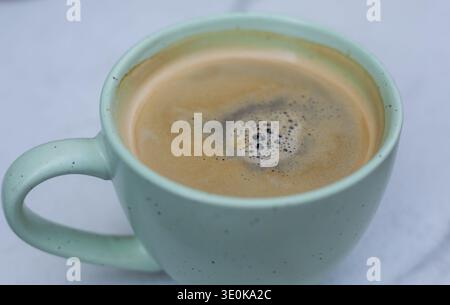 top-down view of a steaming cup of freshly brewed black coffee with rich crema and central bubbles in a dappled mint green ceramic mug on a light grey Stock Photo