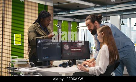Young programmer in office requests help from IT experts detecting and blocking hacker intrusion. Intern assisted by staff members coordinating incident response for network attack, camera A Stock Photo