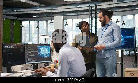 Teamworking programmers in office reviewing AI system metrics, monitoring performance dashboards. Tech company coworkers tuning neural networks using tools on laptop, camera A Stock Photo