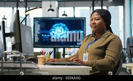 Female technician using computer to write code, developing machine learning APIs. African american woman troubleshooting software errors and faults using artificial intelligence, camera A Stock Photo