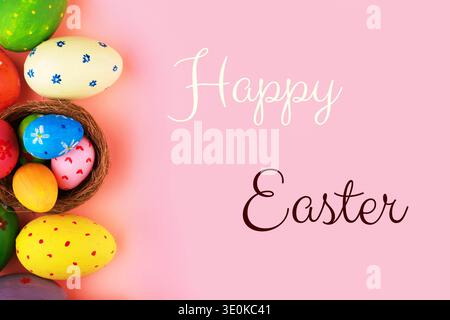 Happy Easter greeting card featuring colorful hand-painted eggs in a nest and forming a decorative border on a pastel pink background. Flat lay compos Stock Photo
