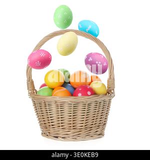Bright Easter eggs falling into basket on white background Stock Photo