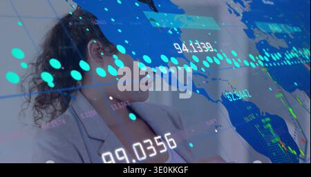 Mid-adult woman wearing gray blazer studying digital world map at office, with teal data points Stock Photo