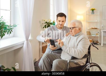 Elderly Patient In Wheelchair With Nurse Spending Leisure Time Using Phone Stock Photo