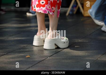 BANGKOK, THAILAND-FEB 22, 2026: Woman in high heel rubber shoes standing on pavement, colorful floral dress, high angle view Stock Photo