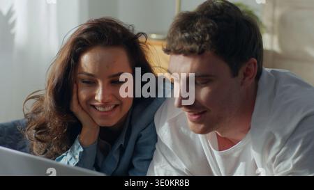 Happy Caucasian couple man woman laughing together at home using laptop computer smiling love technology talking discussing watching movie Stock Photo