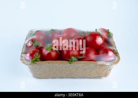 Fresh red cherry tomatoes packed in a sustainable cardboard tray with plastic film wrap Stock Photo