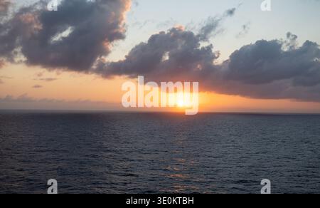 Golden sunset over the Caribbean Sea with dramatic clouds and glowing sunlight reflecting across the ocean horizon. Stock Photo