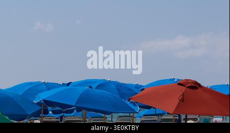 Colorful blue beach umbrellas with a single red umbrella on a tropical beach in Grand Cayman, Cayman Islands, Caribbean. Stock Photo
