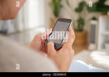 Person holds a broken smartphone in a living room setting Stock Photo