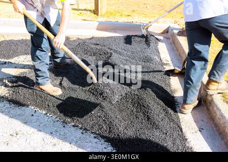 Two workers place hot asphalt on parking lot surface using shovels rakes during road work Stock Photo