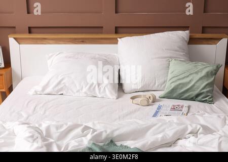 Headphones with newspaper on unmade bed in hotel room Stock Photo