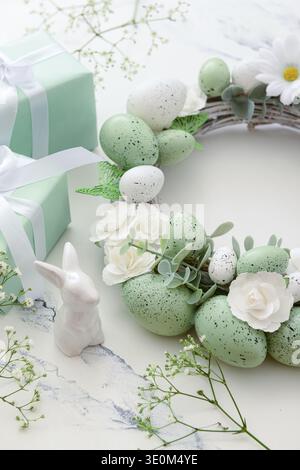 Composition with Easter wreath made of green painted eggs and bunny figurine and gifts on white table Stock Photo