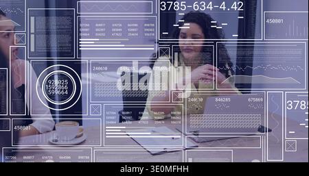 Listening curly-haired woman in sweater holding hands near chin in office, with laptop and overlays Stock Photo