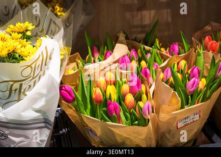RIGA, LATVIA. 12th March 2026. Close up of vibrant pink, orange, and yellow tulips wrapped in eco-friendly brown paper. New LIDL store opening. Stock Photo