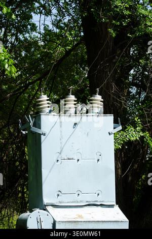 High voltage electrical transformer with ceramic insulators in a rural area. Power supply and electrical infrastructure.  Old grey power transformer b Stock Photo