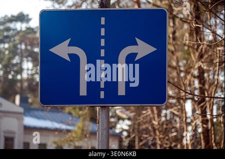 A road sign indicates possible left and right turns in a wooded area near a building. Stock Photo