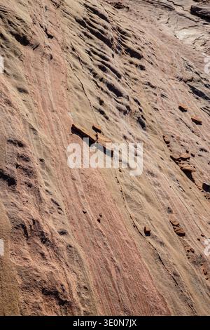 Layered sandstone rock surface with natural erosion patterns and sediment lines on sloping desert cliff face. Stock Photo
