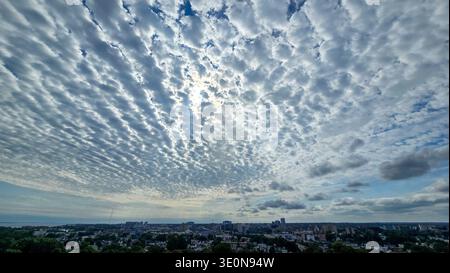 Wide city skyline under dramatic textured cloud pattern with sunlight breaking through bright sky. Stock Photo