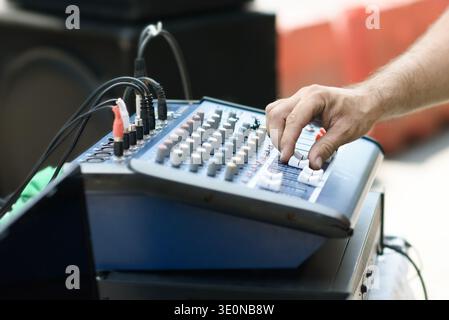 Hand adjusting faders on audio mixer with cables and control knobs for live sound, music production and event audio. Stock Photo