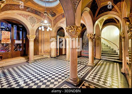 Visitors enter a grand hall with columns and arches. The checkered floor contrasts with the painted ceiling and chandelier. Stock Photo