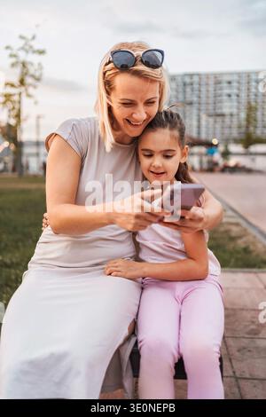 Mother and daughter using smartphone and smiling in a park Stock Photo