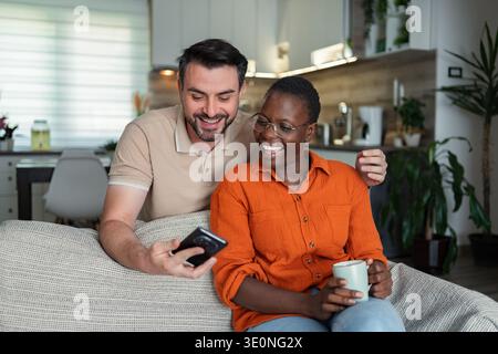 Happy couple laughing and using smartphone at home Stock Photo