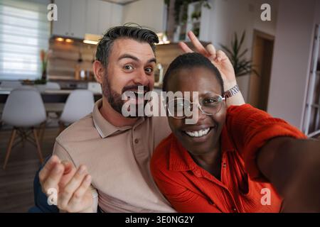 Playful Couple Taking a Selfie at Home, Making Funny Faces Stock Photo