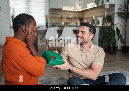 Man surprising his girlfriend with a gift at home Stock Photo