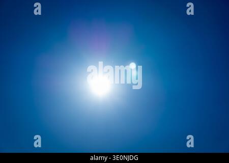 Bright sun shining in a clear blue sky with visible halo and lens flare. Stock Photo