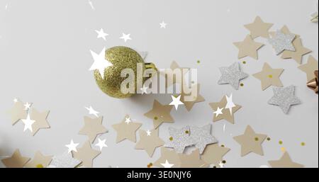 Resting gold glitter bauble on white flatlay, surrounding beige and silver star confetti, metal bow Stock Photo