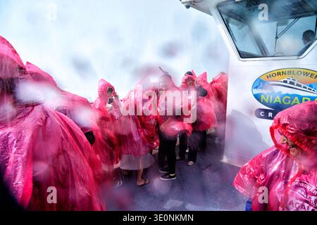 Tourists in pink ponchos on a Hornblower Niagara Cruises boat get soaked by the mist of Niagara Falls, enjoying the close-up experience. Stock Photo