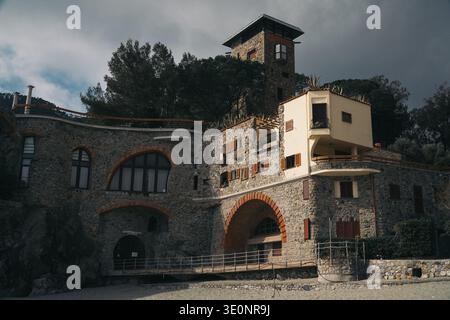 Villa Mondine, Monterosso al Mare, Italy. Historic stone coastal structure with modern elements and tower under dark sky. Stock Photo