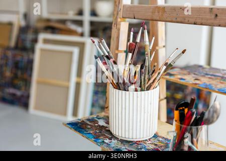 Paintbrushes in white vase on easel in art studio Stock Photo