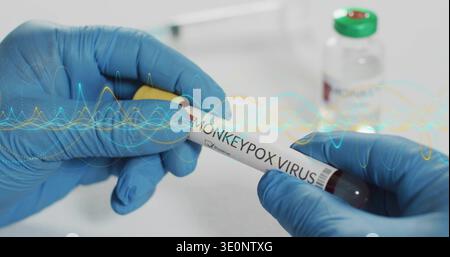 Holding blue nitrile gloves showing blood tube labeled MONKEYPOX VIRUS on lab bench, waveform Stock Photo